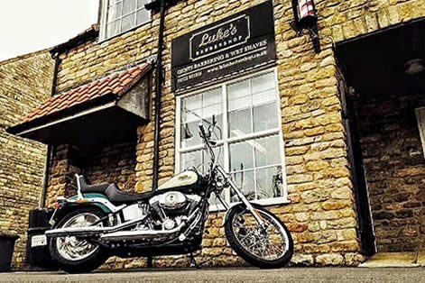 The stone-fronted Luke's Barbershop on Navenby High Street, with a motorbike parked outside.